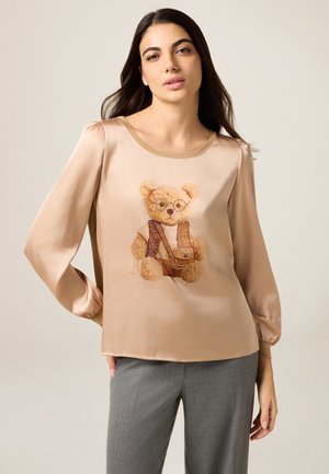 Top beige in satin a manica lunga con grafica di un orsetto con occhiali e gilet a motivo. Tessuto liscio, scollo arrotondato e polsini aderenti.