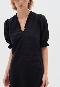 Schwarzes Leinenkleid mit tiefem V-Ausschnitt, gerüschtem Saum und puffärmel mit elastischen Bündchen. Glatte Textur, knielanges Design.