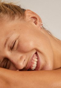 Orecchini a cerchio argento con un design curvo, indossati all'orecchio di un modello, che evidenziano una superficie liscia e riflettente.