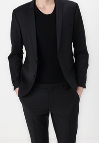 Svart kavaj med matchande byxor, tillsammans med en figurnära svart stickad skjorta. Har en stilren design och en mjuk textur.