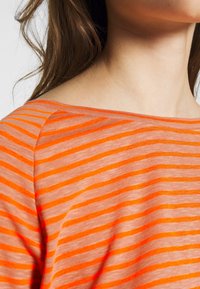 Orange randig topp med en bred halsringning och mjukt, lätt tyg med horisontella linjer i varierande nyanser av orange.