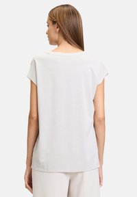 Jasnoszara bluzka z krótkim rękawem o luźnym kroju, z okrągłym dekoltem i gładką, miękką teksturą. Subtelne różowe akcenty w okolicy ramion.