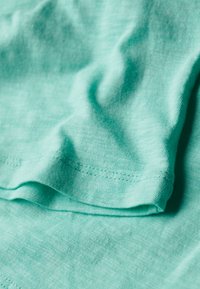 Campione di tessuto turchese con una texture liscia; presenta morbide pieghe e una leggera lucentezza, mostrando un design semplice senza motivi o decorazioni.