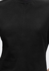 Κοντινή λήψη μιας μαύρης υφασμάτινης μπλούζας με λεπτή κεντρική ραφή και ελαφρώς στρογγυλεμένο λαιμό.