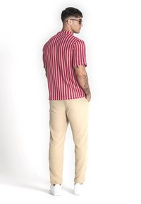 Rood en wit gestreepte korte mouwen shirt, gecombineerd met beige broek. Het shirt heeft een gekraagde halslijn, textuurstof en een relaxte pasvorm.