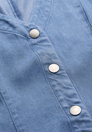 Blåt denimstof med tre runde sølvfarvede trykknapper, der er justeret lodret langs den syede stolpelukning.