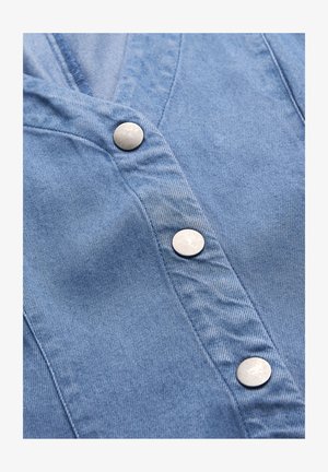 Blåt denimstof med tre runde sølvfarvede trykknapper, der er justeret lodret langs den syede stolpelukning.