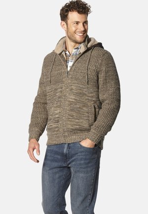 Strickjacke mit Kapuze in Brauntönen, mit einem Reißverschluss vorne, strukturiertem Stoff und Seitentaschen. Getragen über einem karierten Hemd, mit einem weichen Innenfutter.