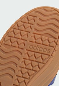 Podeszwa buta Adidas w jasnobrązowym kolorze z wzorzystą powierzchnią, zawierająca trójkątne i faliste tekstury oraz wytłoczone logo marki.
