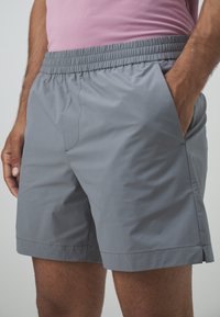 Pantalones cortos grises hechos de un material ligero con una cintura elástica, bolsillos laterales y un diseño simple. Tienen un corte recto en la parte inferior.