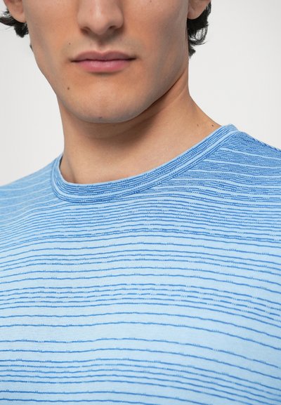 Gaiši zila īsroku krekls ar smalkām horizontālām svītrām tumšākā zilā krāsā. Apaļa kakla izgriezums un mīksts, teksturēts audums.