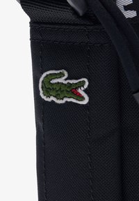 Dettaglio di una borsa di stoffa nera con un logo di coccodrillo ricamato in verde e bocca rossa, che mette in evidenza la texture e le cuciture del materiale.