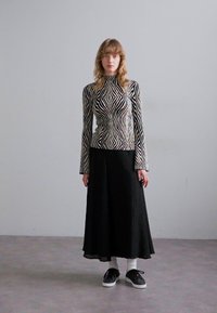 Sudadera de manga larga en blanco y negro con un patrón de zigzag, combinada con una falda larga plisada negra y zapatillas negras. Medias blancas visibles.