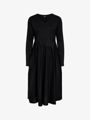 Musta mekko, jossa on V-aukko ja pitkät hihat, yläosa istuu hyvin ja alaosa on pehmeästä kankaasta laskeutuva ja liehukeva.