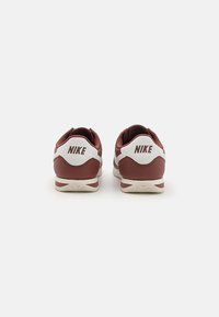Punane ja valge Nike kets, millel on sile nahast ülemine osa, pehmendatud krae, ümar varvas ja tekstuuriga valge välistald, millel on mustriline serv.
