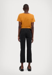 Black cropped jeans with a straight cut, paired with a short-sleeved mustard shirt. The outfit is completed with black platform shoes.