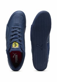 Chaussures de sport en cuir bleu avec une semelle texturée, arborant un logo Ferrari jaune sur la languette et des accents blancs le long des côtés.