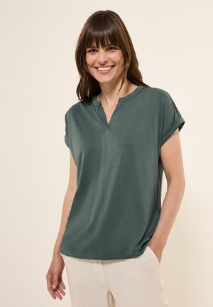 Haut vert foncé à manches courtes avec un col en V et des revers. Fabriqué en tissu doux, présentant une coupe décontractée et des poches sur les côtés.