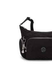 Schwarze Tasche mit strukturiertem Muster, ausgestattet mit silbernen Reißverschlüssen, abnehmbarem Trageriemen und dekorativen Schlüsselanhängern an der Vorderseite.