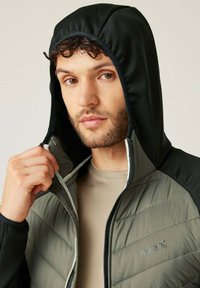 Kapuzenshirt mit schwarzem Oberteil und leicht olivfarbenem, gestepptem Körper. Verfügt über einen durchgehenden Reißverschluss, strukturierten Stoff und Logo der Marke auf der Brust.