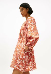 Robe fleurie rouge et blanche, avec manches longues, taille cintrée et poches latérales, confectionnée dans un tissu léger à motif texturé.