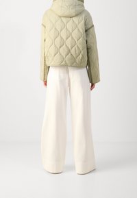 Veste matelassée vert clair avec capuche, présentant un motif texturé, associée à un pantalon large couleur blanc cassé.
