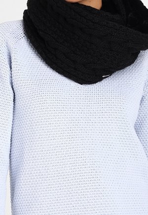 Personne portant un pull en maille texturée bleu clair et une grosse écharpe infinity tricotée noire autour du cou.