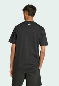 Sort bomulds T-shirt med korte ærmer, rund hals, og hvid Adidas-logo på ryggen. Løs pasform og glat tekstur.