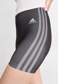 Juodi sportiniai šortai, pagaminti iš tamprios medžiagos, turi tris baltas juosteles šonuose ir „Adidas“ logotipą ant juosmens.