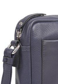 Navy Leder Tasche mit strukturiertem Finish, ausgestattet mit einem silbernen Metallreißverschluss und -beschlägen sowie einem verstellbaren Schultergurt.