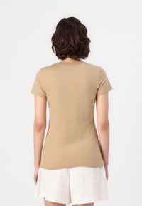 Short-sleeve, fitted t-shirt in light brown cotton with a crew neckline, viewed from the back, featuring a smooth texture and simple design.