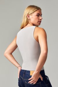 Light gray sleeveless top with a fitted design and smooth texture, paired with dark blue jeans featuring a tan leather patch on the back.