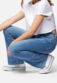 Vaqueros de campana de denim azul claro con un acabado desgastado, combinados con una camiseta blanca cropped básica y zapatillas blancas con rayas negras.