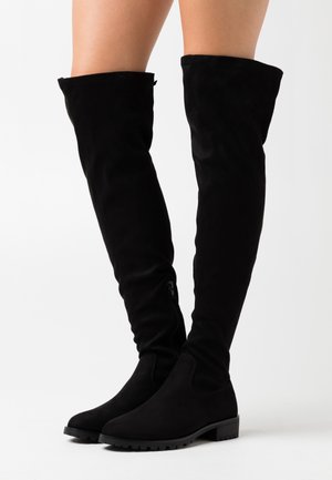 Botas negras de ante hasta la rodilla con punta redonda, que cuentan con una cremallera lateral y un tejido texturizado. Suela plana con un tacón bajo tipo bloque.