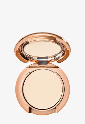 Poudre compacte avec une surface lisse de beige pâle, contenue dans un boîtier rond en métal rose doré réfléchissant, avec un couvercle clair et une charnière.
