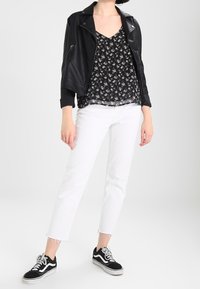 Czarna skórzana kurtka motocyklowa na czarnej kwiatowej bluzce, zestawiona z białymi krótkimi dżinsami i czarnymi trampkami z białymi podeszwami i sznurówkami.