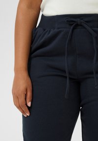 Pantaloni della tuta blu navy realizzati in tessuto morbido, dotati di un cinturino elastico con lacci e tasche laterali.
