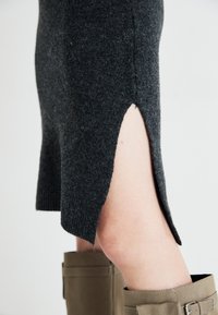 Gray knitted dress featuring a side slit, textured fabric, and a straight hem. Paired with beige knee-high boots.
