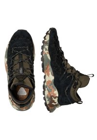 Bottes courtes en daim noir et textile vert avec semelle en caoutchouc à motif camouflage. Elles comportent des lacets texturés et un logo hexagonal sur la languette.