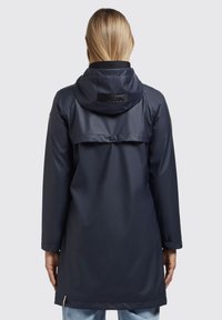 Parka impermeable marina con capucha, que cuenta con un yugo trasero, mangas largas, cierre a presión y una textura suave y brillante.