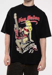 Black cotton t-shirt featuring a graphic of a woman in a red outfit holding a patterned guitar, with "Van Halen" and "Running with the Devil" text.