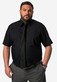 Svart kortärmad skjorta med krage och framficka, kombinerad med svart slips och grå byxor. Har slätt tyg och en strukturerad design.