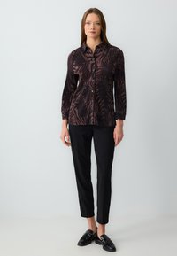 Camicia a maniche lunghe con bottoni di colore viola scuro con un motivo ondulato nero, abbinata a pantaloni neri e scarpe nere. Tessuto dalla consistenza liscia.