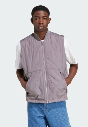 Vadderad grå väst med blixtlåsförslutning, sidfickor och ribbad krage, bärs över en vit skjorta och matchas med blå mönstrade jeans.