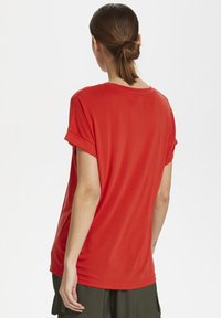 Red, short-sleeve t-shirt with a loose fit, featuring rolled cuffs and a round neckline, made from soft, smooth fabric.