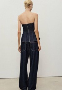 Denim peplum-paita ja leveälahkeiset farkut tummassa pesussa. Paita on muotoiltu ja siinä on vetoketj closure, ja farkuissa on kaksi takataskua.