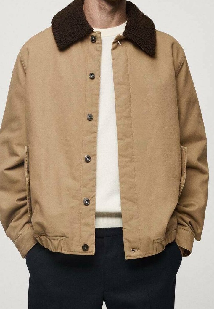 Beżowa kurtka z brązowym, teksturowanym kołnierzem. Posiada zapięcie na guziki, boczne kieszenie oraz luźny fason. Noszona na lekkim swetrze.