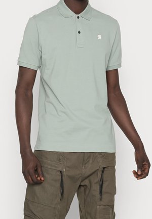 Polo vert clair avec un col classique, des manches courtes et un petit logo sur la poitrine. Porté avec un pantalon cargo olive équipé de fermetures éclair.