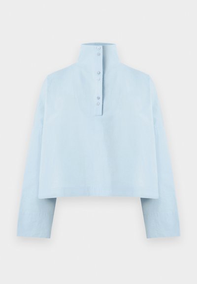 Light blue cropped shirt with a high collar, long sleeves, and five-button closure at the back. Made from a smooth, textured fabric.