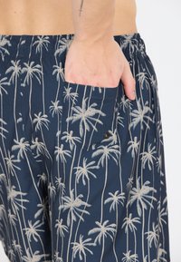Marineblaue Shorts aus leichtem Stoff mit einem cremefarbenen Palmenmuster. Elastischer Bund mit Seitentasche und Knopfdetail.